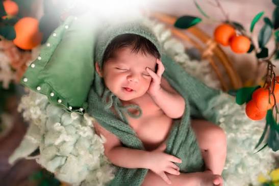Newborn resting in a soft green wrap beneath orange branches